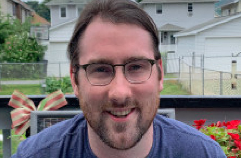 Closeup of a man smiling in a blue t-shirt with houses in the background